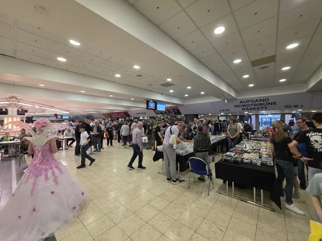 The foyer of the Grugahalle during the Lego-Börse: visitors at long tables of loose minifigures, a cosplayer in a pink and white gown in the foreground