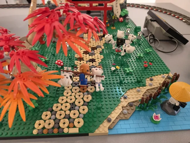 A Japanese-themed LEGO landscape with red and orange maple trees, stepping stones, a red torii gate and small white creatures on the grass